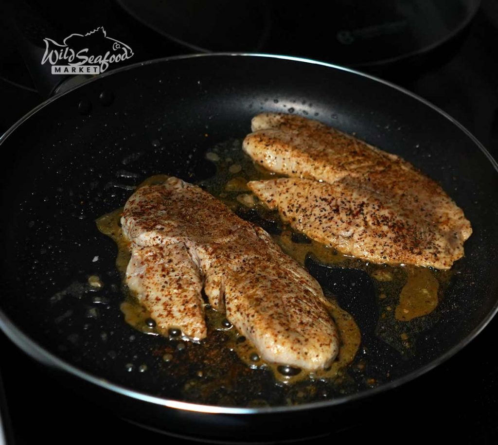 Cooking snapper in the pan with seasoning atop it
